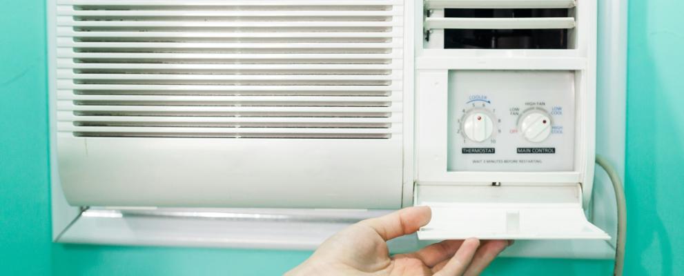 Eine Hand öffnet das Bedienfeld zu einer Klimaanlage